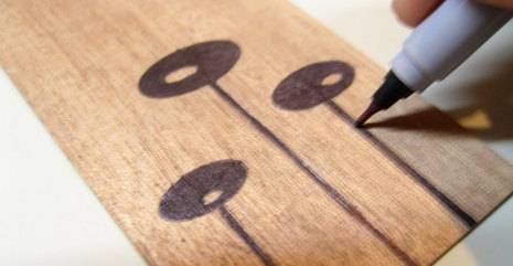 Drawing three stem pods on a piece of wood with a thin black sharpie.