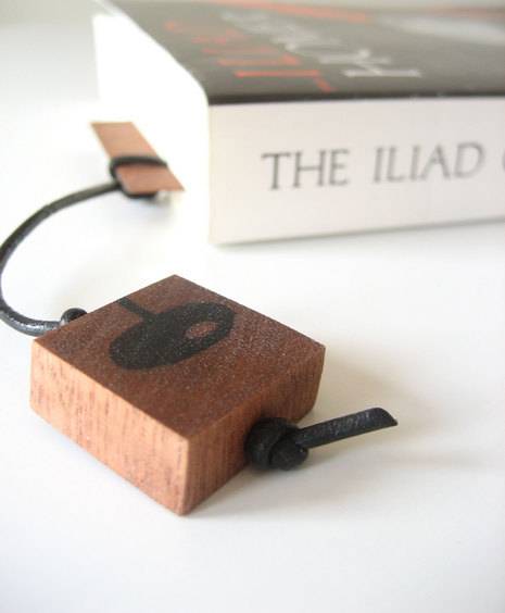 A block of wood attached by a cable to a flat piece of wood operating as a bookmark sticking out of a paperback book.