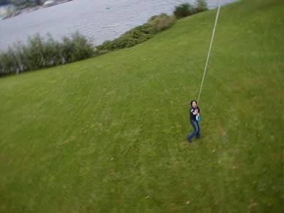 Aerial view of a person holding a kite string while walking on a large grassy area next to a lake.