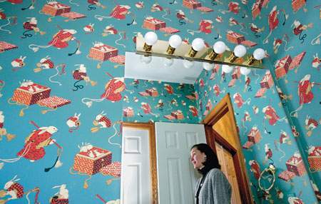 A woman in standing in a door in a room with blue Christmas wall paper.