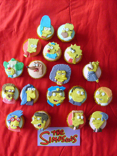 Multiple Simpson cupcakes on red cloth.