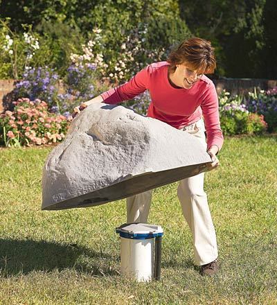 A woman in a red shirt lifting a rock over a cannister.