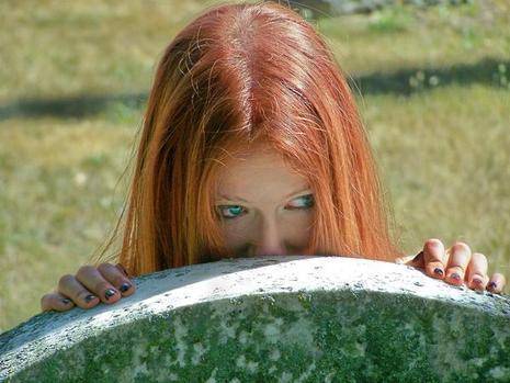 Red haired woman peaking from behind a stone.