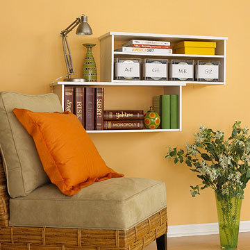 A sitting room that has several free hanging book cases and a chair with an orange pillow.