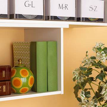 A white shelf with two green books, a green and orange ball and two brown books.