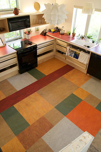 A kitchen with a colorful grid floor with a black stove and white countertops.