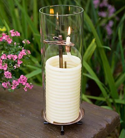 A glass and white candle holder is sitting outside on a wooden table.
