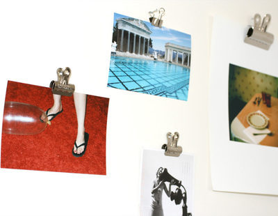 "A collection of photos clipped on the white wall with bulldog clips."