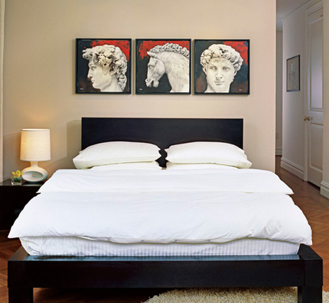 Three pieces of Roman artwork hang above a black and white bed.