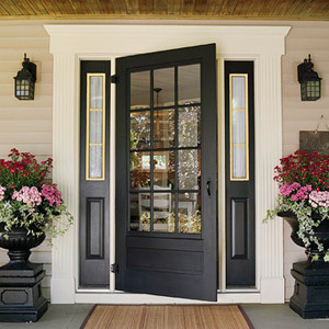 Solid wooden front door painted black and with large flower vases on each side.