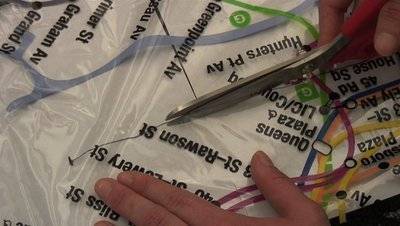 A person's hand cutting a transparent map with a pair of scissors.