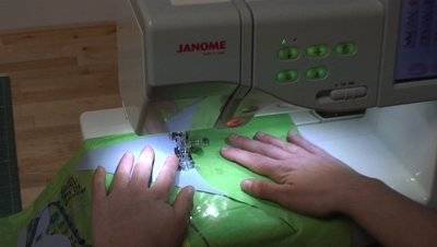 A person is running green material under a sewing machine.