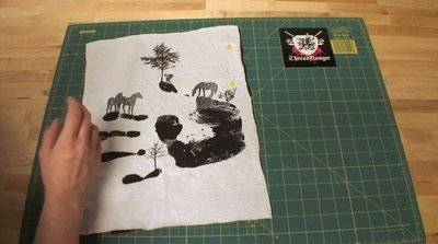 A white piece of cloth with grey horses and a handprint on it on top of a green cutting mat.