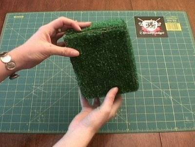A person is holding a cube of grass near a grid.