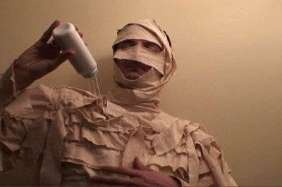 A person dressed as a mummy is pouring something on themselves.
