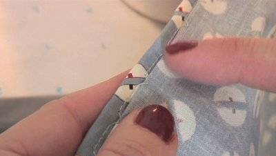 Woman showing blind hem stitch on fabric edge with hands.