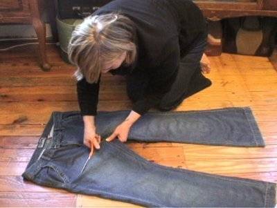A woman knelt down on the floor cutting the legs off a pair of jeans.