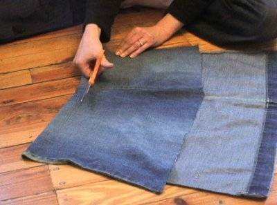Blue denim fabric being cut with orange scissors on top of other fabric.