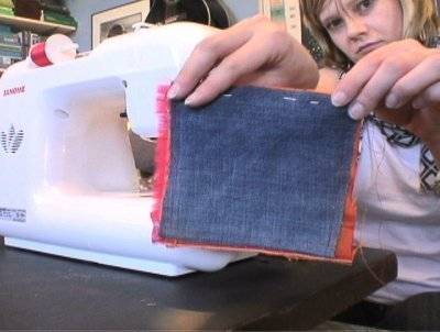 A girl at a sewing machine holding up a piece of jean cloth.