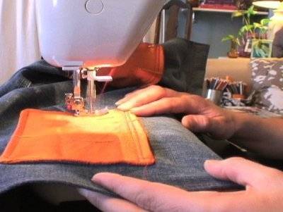 Someone is sewing an orange square of fabric to a grey piece of fabric.