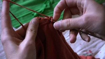 A red cloth being sewed by hand with needles.