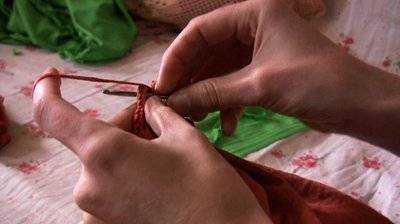 A person crocheting red fabric.