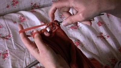 A hand doing some knitting of a brown cloth
