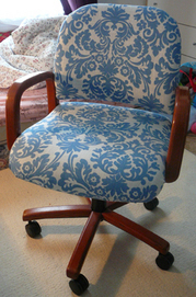A chair that has a white and blue floral design and wood arms and legs.