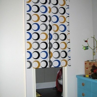 A geometric curtain over the door in a room with a blue dresser.