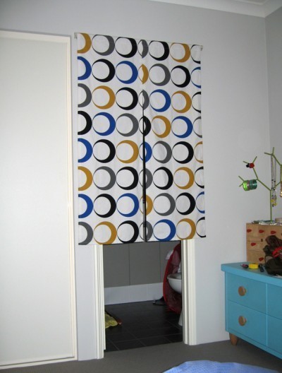 A geometric curtain over the door in a room with a blue dresser.