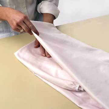 A woman is folding over a pink shirt.