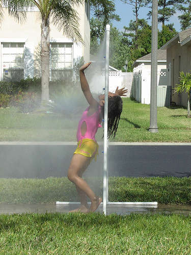 A woman playing in a sprinkler outside in a pink bathing suit.