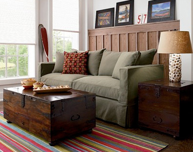 A green sofa is near wooden tables and a striped rug on the floor.