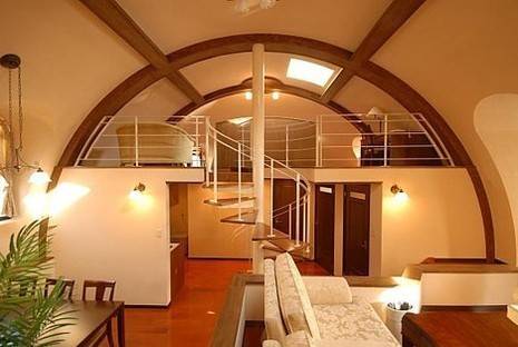 A living room with round opening to a loft and a winding staircase up to it.