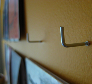 L-shape hooks have been screwed in a wall to display wall art.