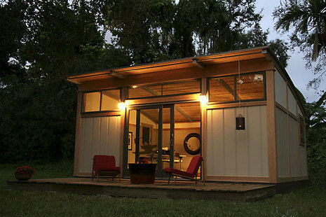 The front of a small cabin, with a pair of chairs and lights on the deck.