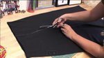 A person cutting a piece of black cloth.