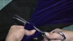 A person cuts blue fabric with metal scissors.