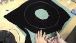 Black fabric on the table being cut by scissors.