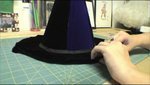 A woman works on the brim of a black witches hat that is on a cutting mat.