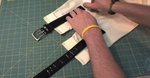 A person is measuring a black belt on a gridded surface.