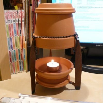 A terra cotta candle burner is sitting near some books.