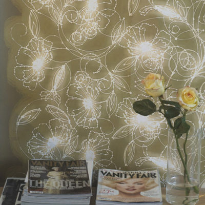 White designs are visible on the tan wall behind a surface holding magazines and a yellow flower.
