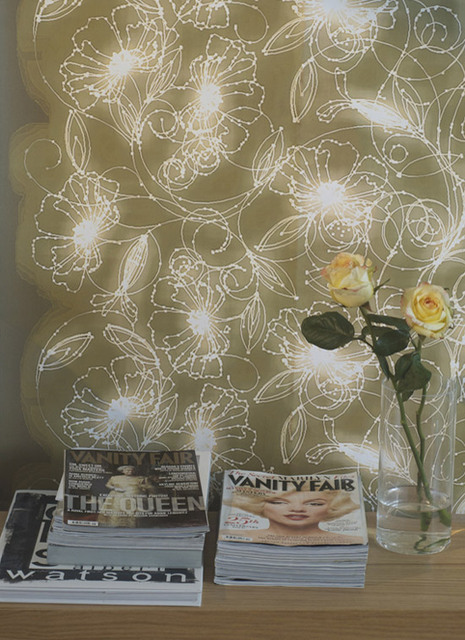 White designs are visible on the tan wall behind a surface holding magazines and a yellow flower.