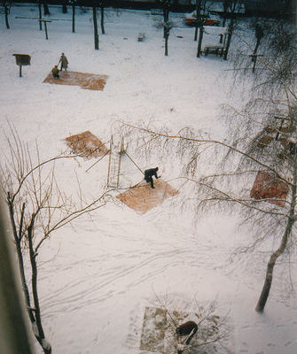 A snowy park with snow covered picnic tables surrounded by bare trees.