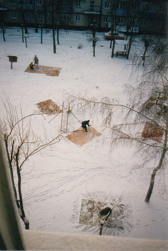 A snowy park with snow covered picnic tables surrounded by bare trees.