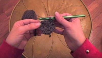 A person is knitting black material with a green needle.