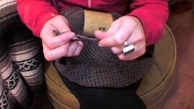 A pair of hands crocheting a brown round which is sitting on her lap.