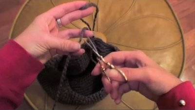 A person cuts purple yarn with metal scissors.