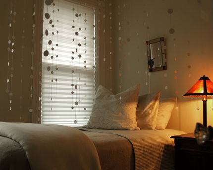 A bedroom contains a twin size bed and hanging strings of paper dials amongst other things.